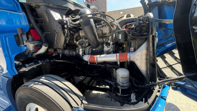 Engine bay of a Freightliner truck showing diesel filter, hoses, and components in view from left side. Visible parts include air intake, hoses, hydraulic lines, and engine bay frame.