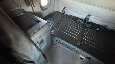 Truck interior showing a folded sleeper bed platform with black straps and surrounding light gray upholstery.