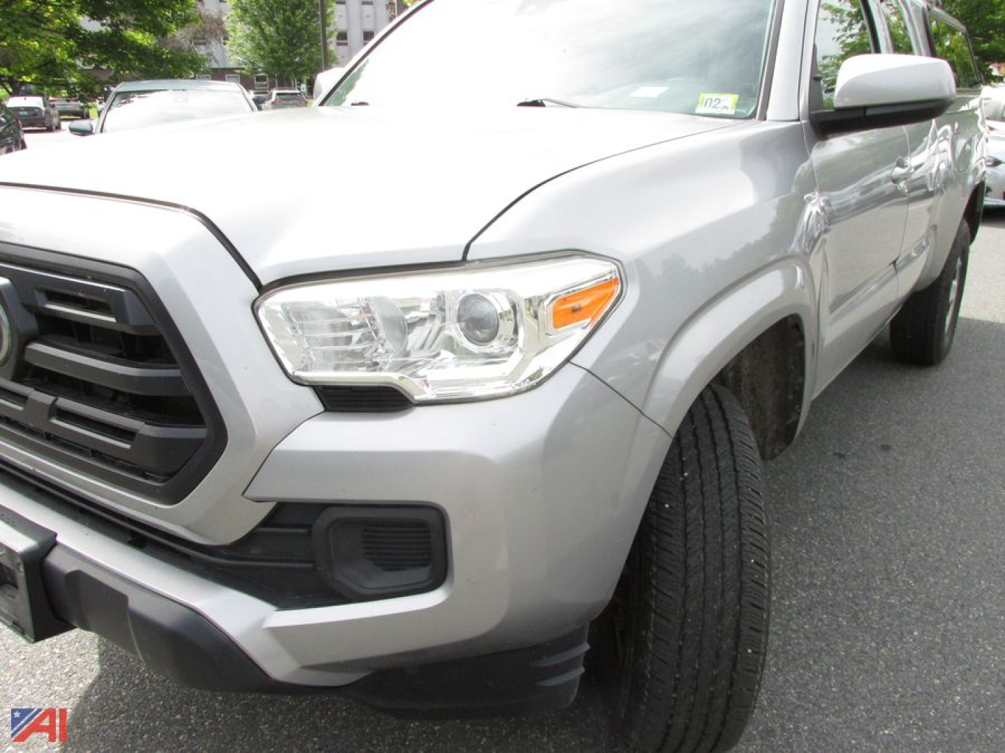 Front-left view of a silver 2018 Toyota Tacoma extended cab pickup truck showing headlight, front grille, and front wheel with tire.
