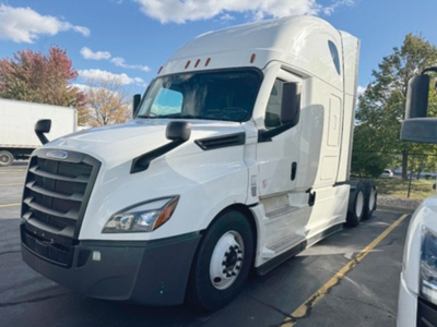 White Freightliner Cascadia126 semi-truck in parking lot with sleeper cab, large front grille, and side mirrors visible.