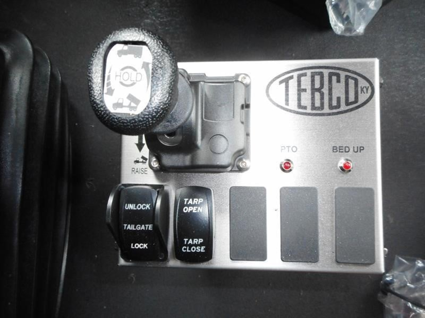 Control panel with Terbo icon and two red indicator lights labeled PTO and BED UP; levers and buttons labeled UNLOCK, TARP OPEN, TARP CLOSE, TAILGATE, LOCK; circular power/engine start knob on left.