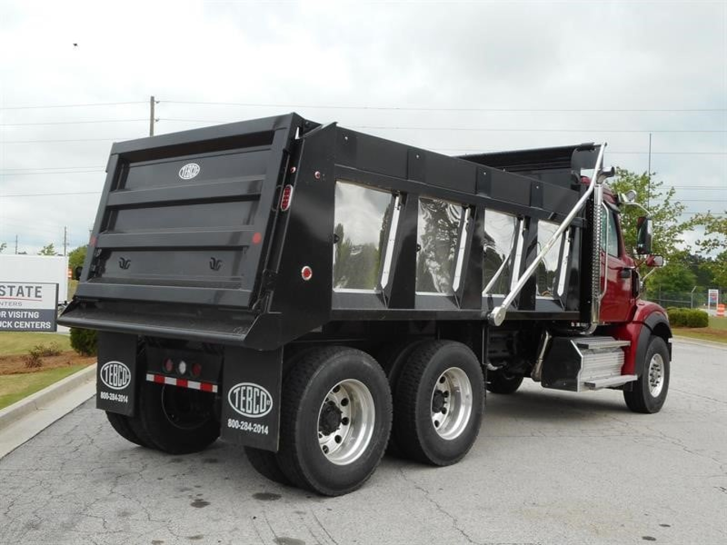 Dump truck rear/side view showing Western Star 47X dump bed, black steel dump body, triple rear axles, red cab, reflective tape, and mud flaps.