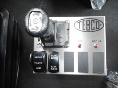Control panel with Terbo icon and two red indicator lights labeled PTO and BED UP; levers and buttons labeled UNLOCK, TARP OPEN, TARP CLOSE, TAILGATE, LOCK; circular power/engine start knob on left.