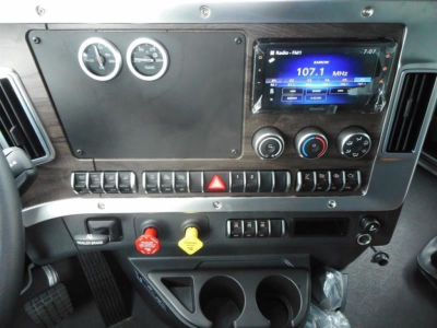 Dashboard of a 2026 Western Star 47X dump truck showing a touchscreen radio, two round gauges, climate controls, and a row of switches; red hazard switch present.