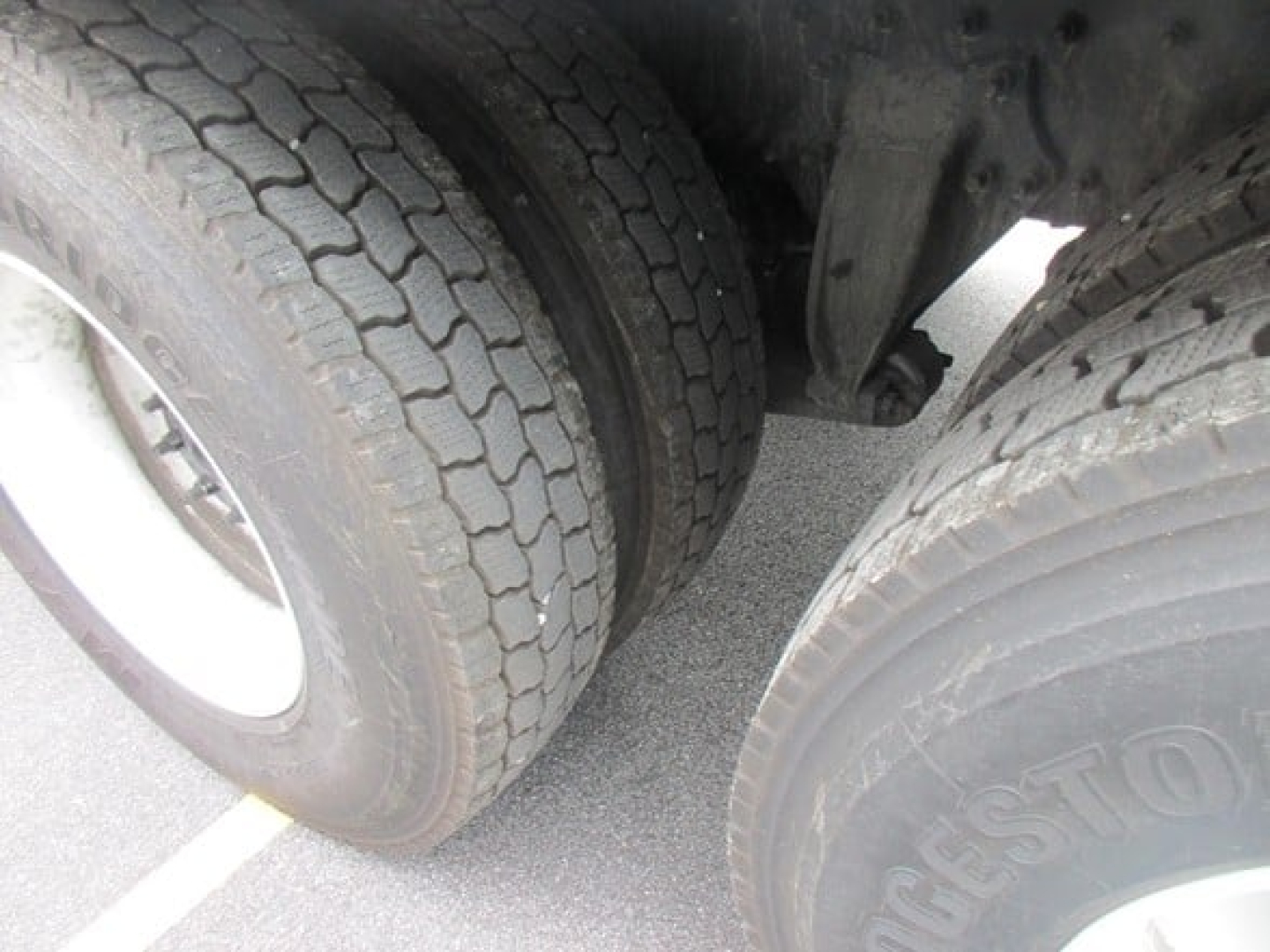 Rear wheel area of a Freightliner M2 106 Plus at a truck show showing dual rear tires and suspension components.