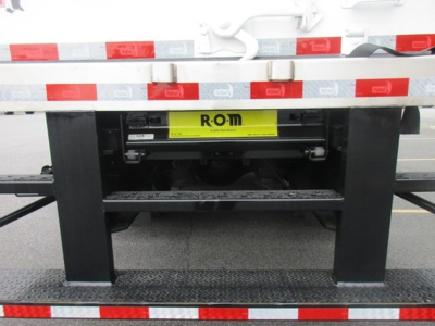 Flatbed/rear view of a Freightliner M2 106 Plus chassis with a yellow ROM placard and undercarriage components visible between the black frame uprights.