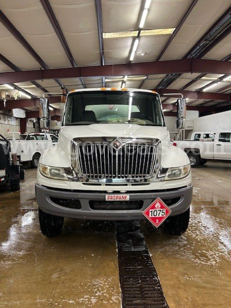 Truck front view of a white 2011 International 4300 tanker in a showroom, with large chrome grille, propane diamond label 1075, and stock plate 12194-13.