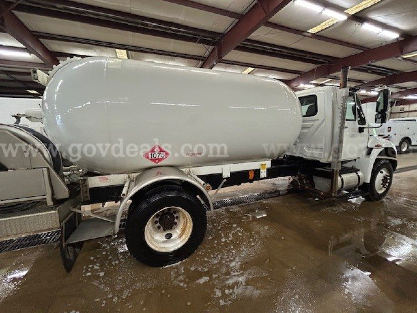 Tank truck with cylindrical tank mounted on chassis, International 4300 cab, water/fuel tank with safety decals visible on side.