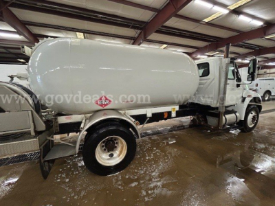 Tank truck with cylindrical tank mounted on chassis, International 4300 cab, water/fuel tank with safety decals visible on side.