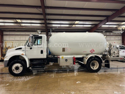 Tank truck showing cylindrical white tanker mounted on International 4300 chassis in a warehouse setting.