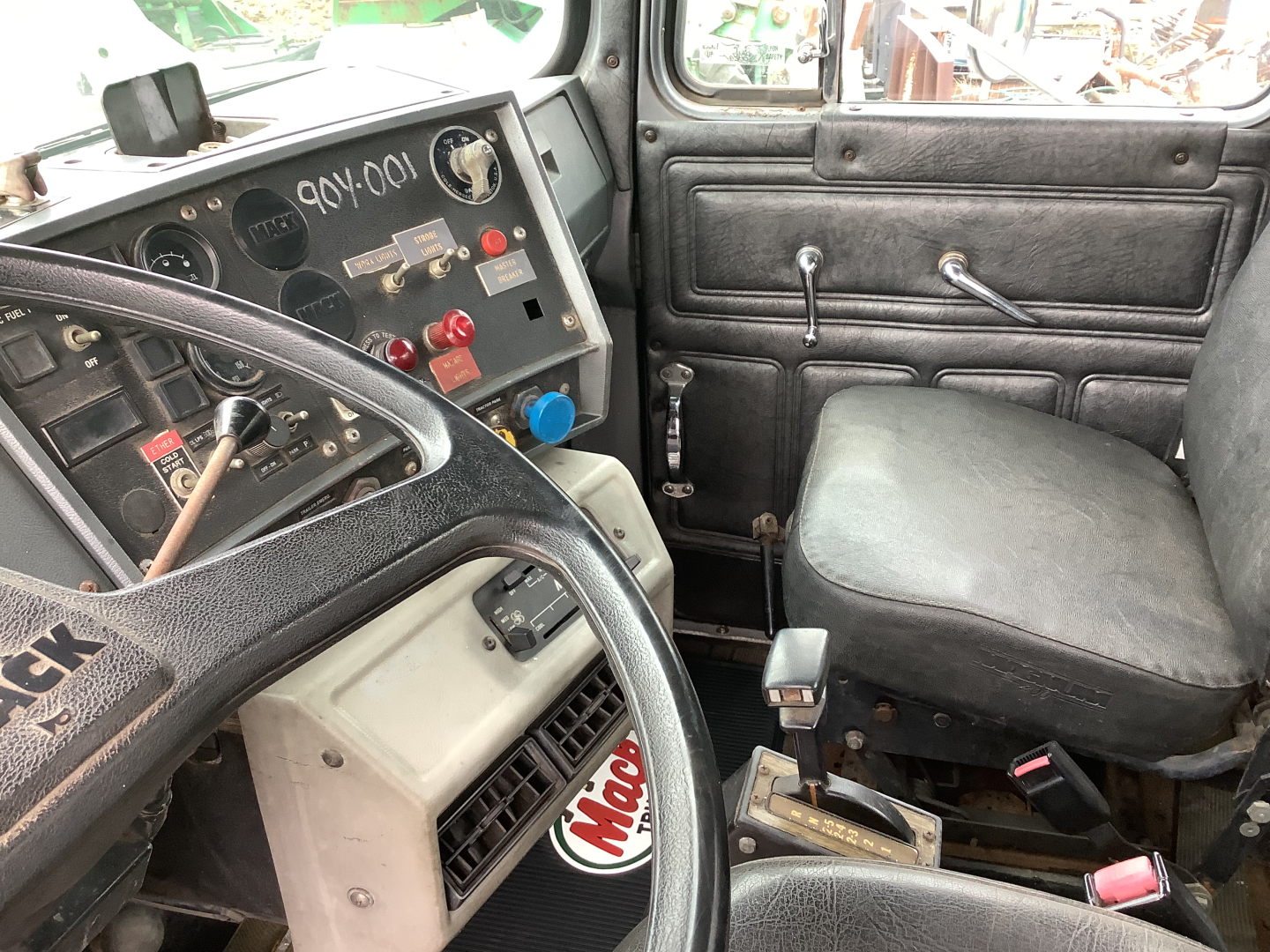 Cab interior of a 1994 Mack RD8 truck showing steering wheel, dashboard with gauges, and manual gear selector; driver seat and door panel visible.