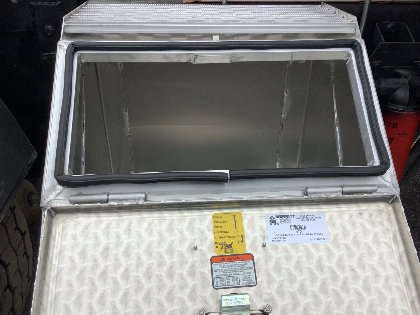 Open refrigerated truck box with interior insulation and labels on the top hatch. Visible text includes a yellow warning tag and a white label with barcodes.