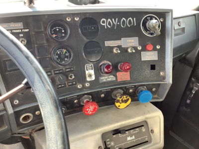 Mack RD8 truck instrument cluster and dashboard controls, various gauges, switches, red and yellow knobs, and steering wheel visible in cab interior.