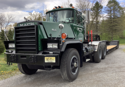 Mack RD8 heavy haul truck with green cab and black grille, front view showing dual rear axles and flatbed trailer.