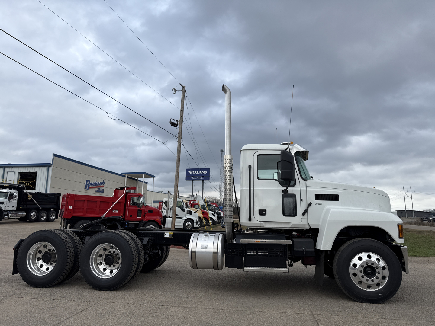 Truck chassis side view showing Mack PI64T tractor with dual rear axles and exhaust stack, white cab, aluminum fuel tanks, and 6-wheel configuration.