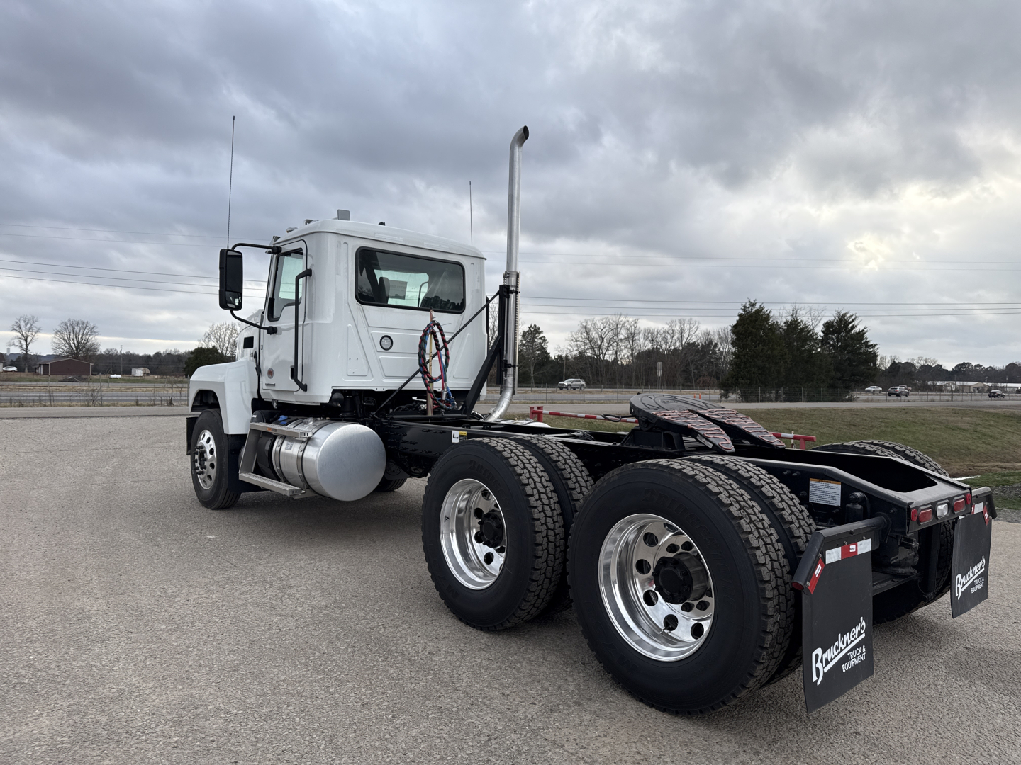 Truck chassis with cab visible, exhaust stack, dual rear axles, white cab, fuel tanks, and fifth wheel area.
