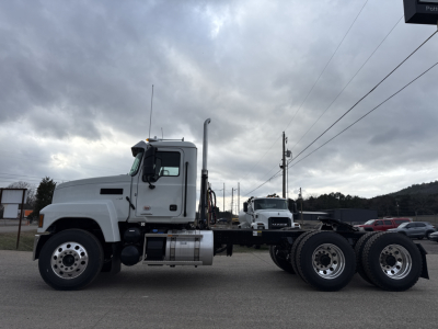 Mack PI64T conventional daycab truck chassis side view showing fuel tank and exhaust stack with triple rear axles in a parking lot.