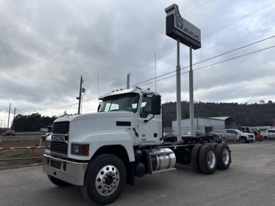 Truck chassis showing Mack PI64T cab over engine with dual rear axles and front grille, white exterior, long wheelbase, in dealership lot.