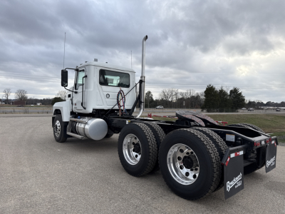 Truck chassis with cab visible, exhaust stack, dual rear axles, white cab, fuel tanks, and fifth wheel area.