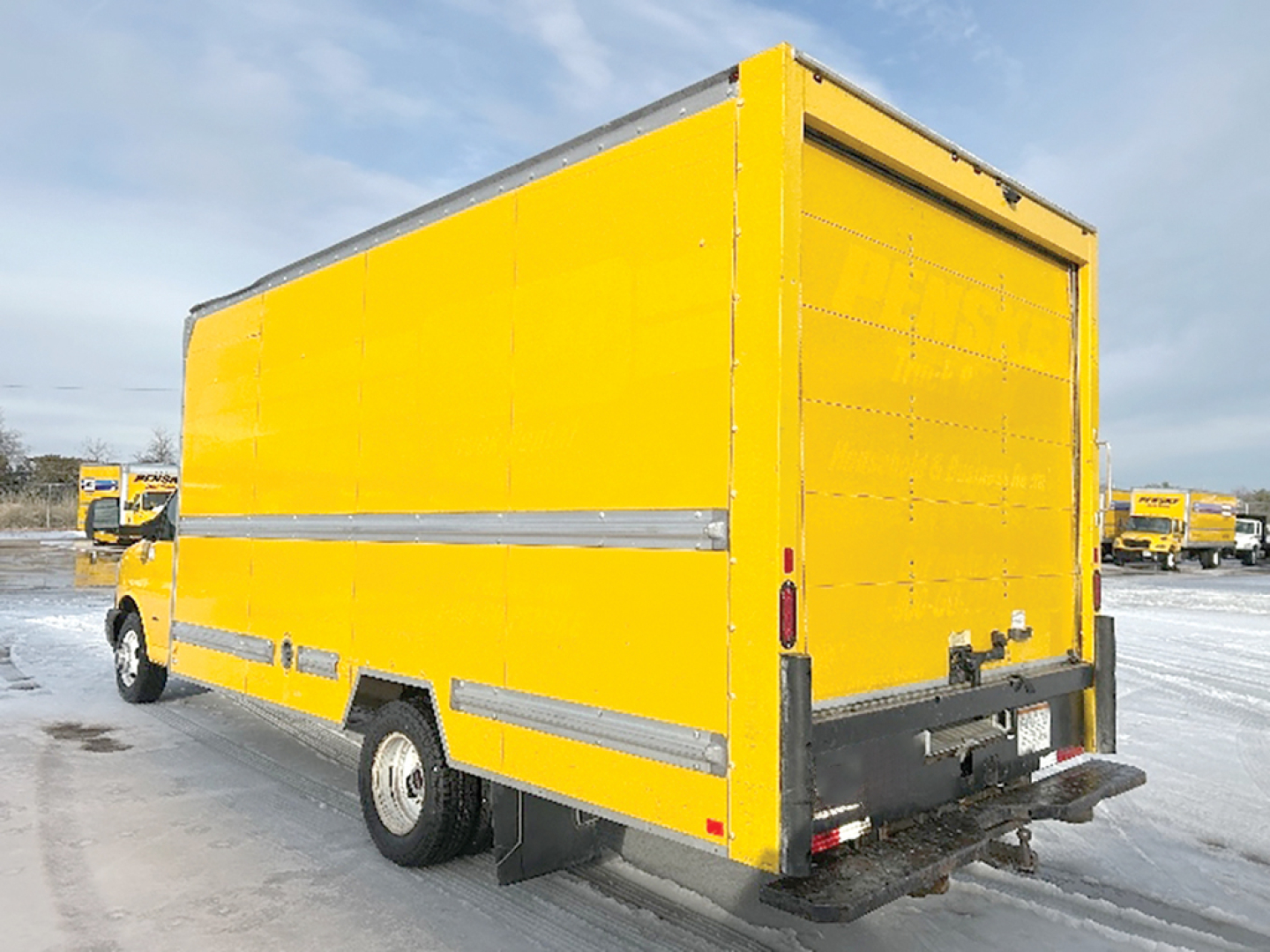 Box truck in yellow with cargo box and rear bumper, side roller rails, winter setting, GMC Savana cargo truck image.