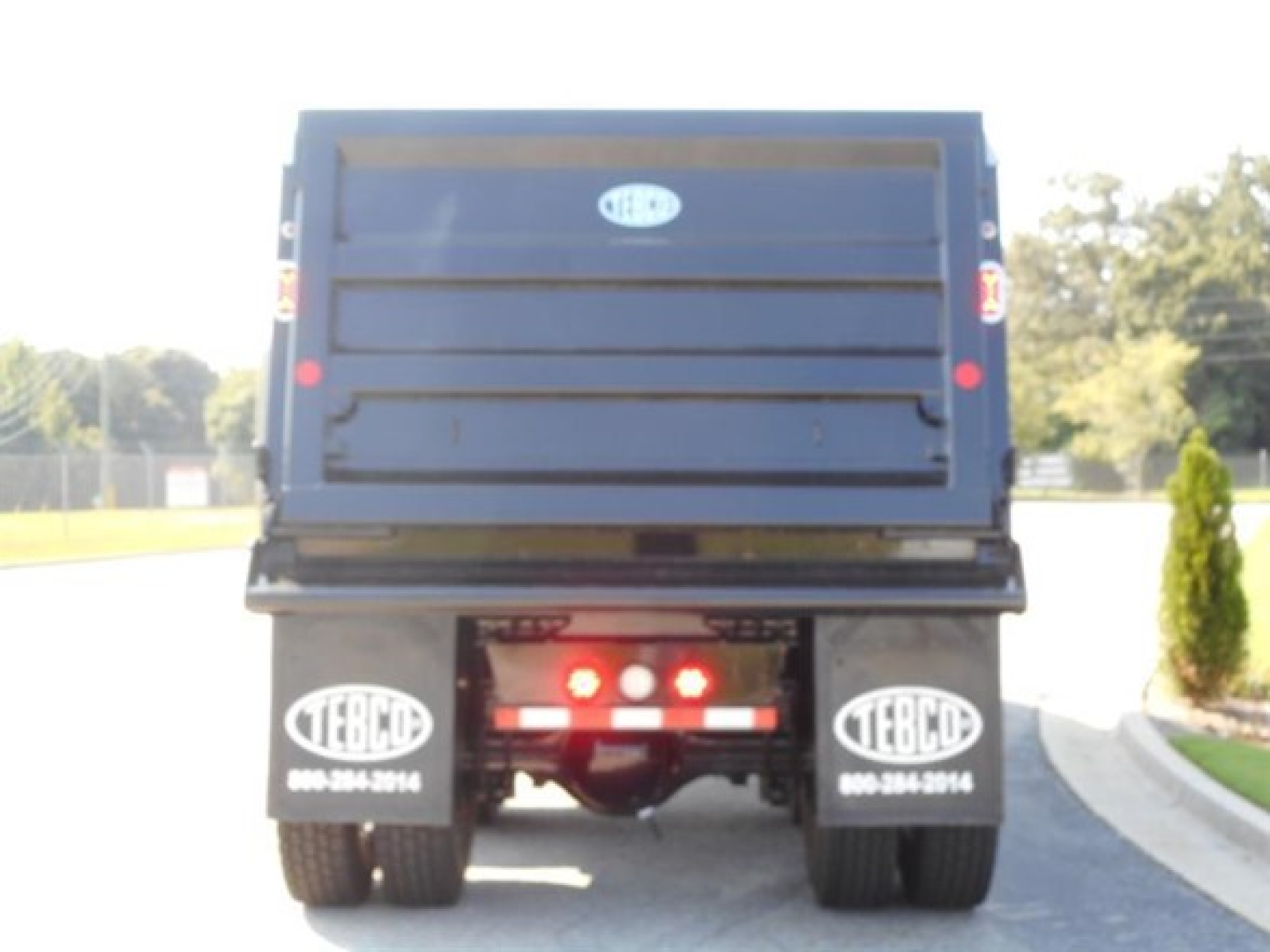 Dump truck rear showing Western Star logo on tailgate and EBCL mudflaps with contact numbers.
