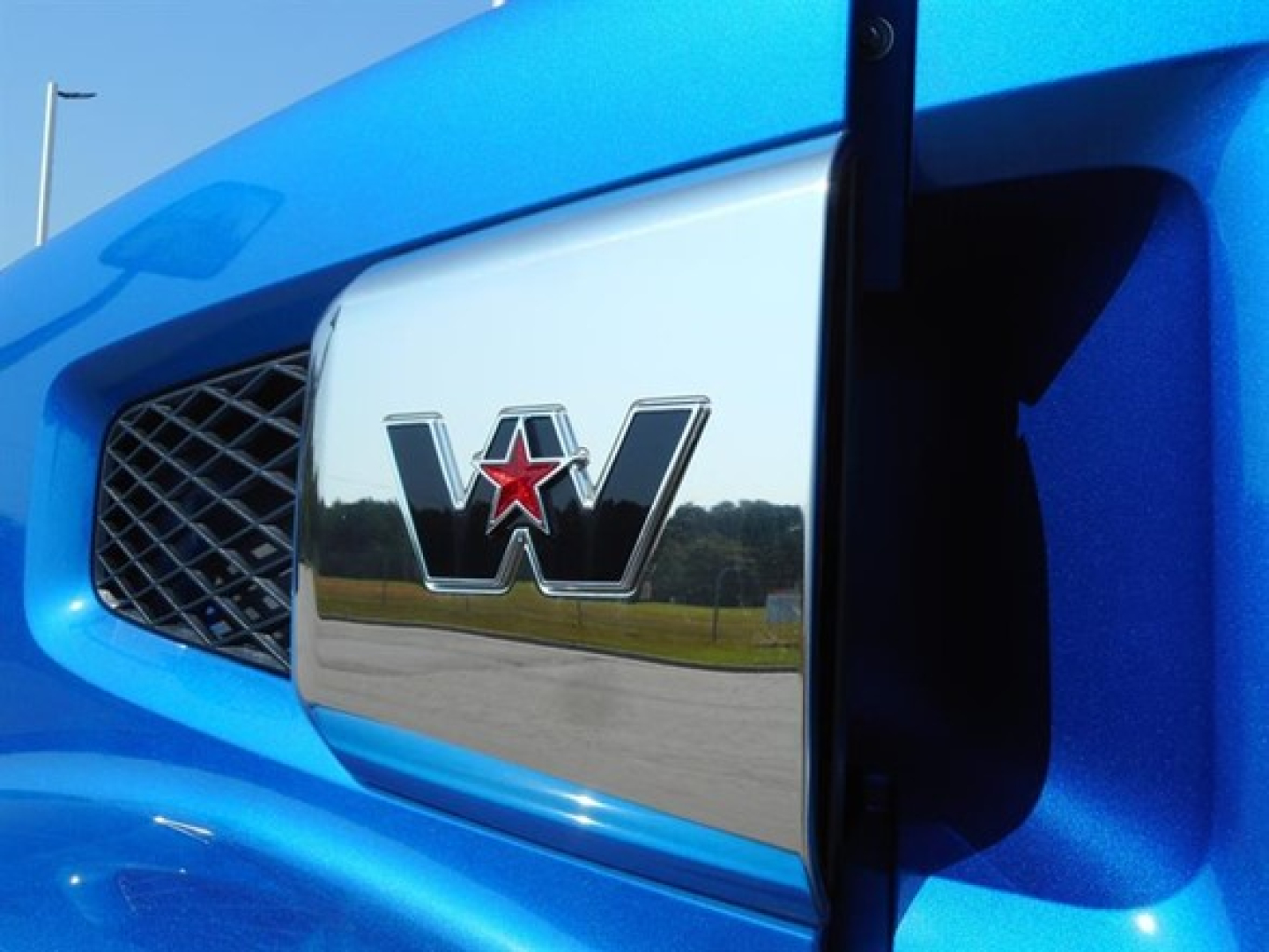 Blue Western Star truck frontend with chrome grille badge showing W emblem and star.