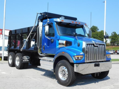 Blue Western Star 47x dump truck front-left view showing chrome grille, dual exhaust, and black dump bed with white dealer sticker.