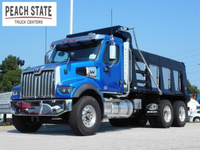 Blue Western Star 47x dump truck in a dealership lot, side view showing chrome bumper, grille, cab, and black dump bed with Peach State Truck Centers logo in background.