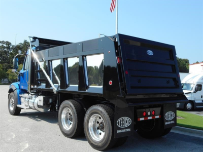 Dump truck showing rear and side view of a blue and black Western Star 47X with black dump bed, dual rear axles, and chrome exhaust stacks.