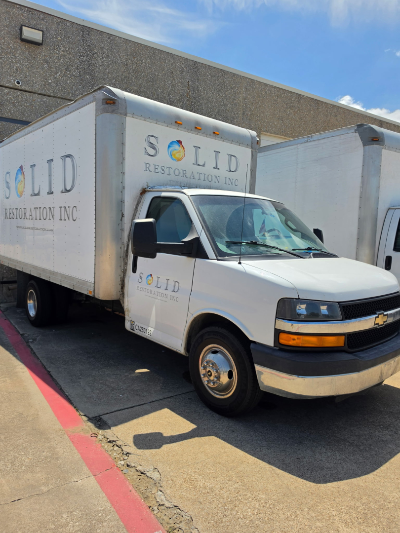 Box truck with SOLID Restoration Inc. branding on cargo box and cab, Chevrolet logo on front grille, side mirrors, and SOLID lettering on the box.