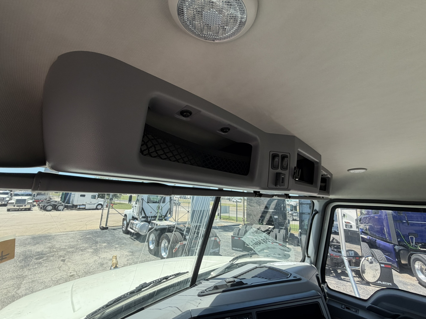 Cab interior overhead console with storage and switches in Mack GR64F cab; window and exterior vehicles visible through windshield.