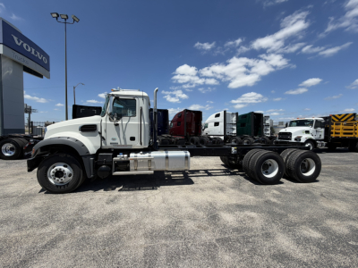 Mack GR64F cab and chassis truck in a dealership lot, side profile, diesel fuel tank, rear axle and wheels visible, other trucks in background.