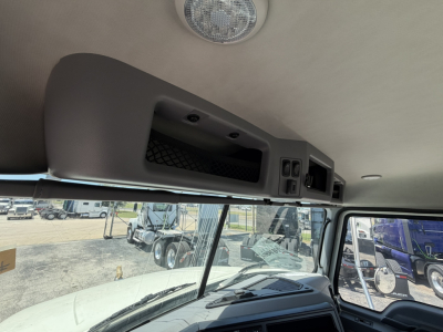 Cab interior overhead console with storage and switches in Mack GR64F cab; window and exterior vehicles visible through windshield.