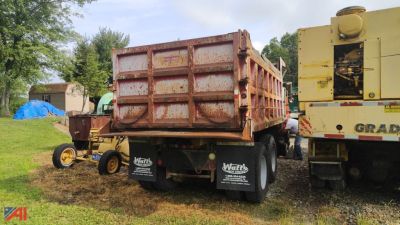 Dump truck bed of a Mack RD690S dump truck with rusted side walls and a yellow crane/loader in the background.