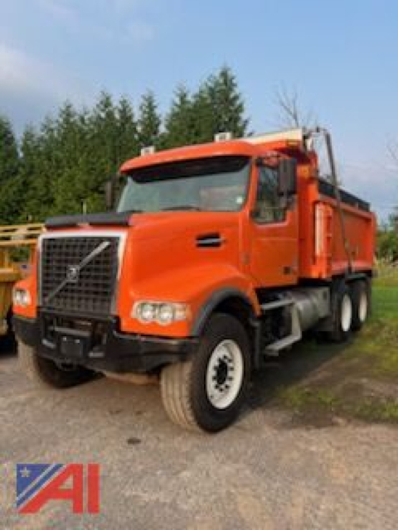 2012 Volvo 10-wheel dump truck front-left view; orange cab with black grille, white wheels, dump bed visible.