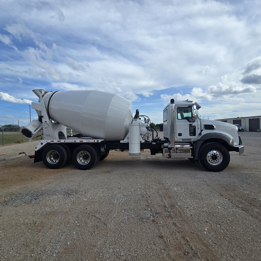 Mixer truck in side view showing concrete mixer drum and chassis with cab at right, blue sky with clouds.