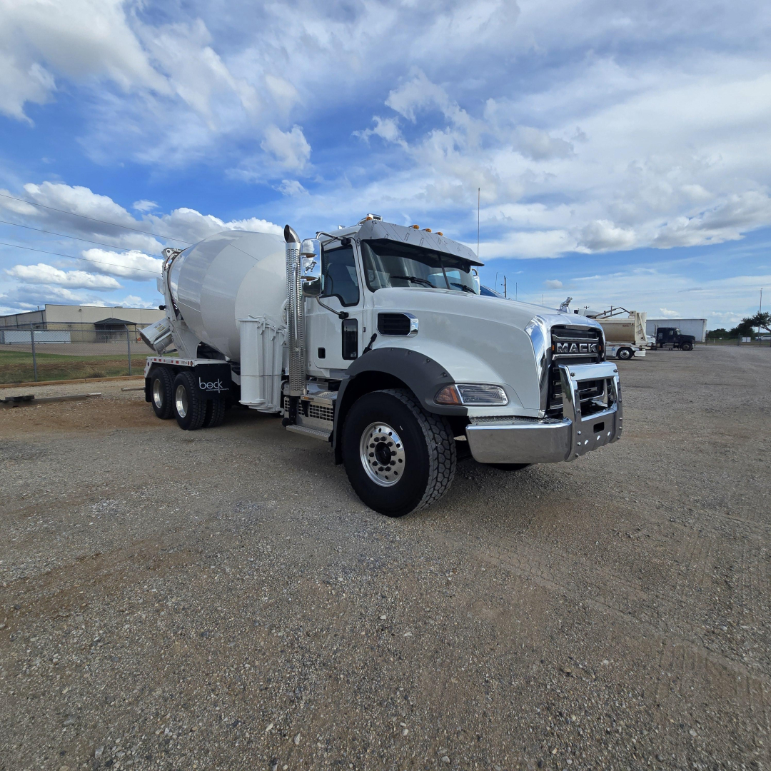 Mack GR64B mixer truck in white, front angled view showing cab and mixer drum on a gravel lot.