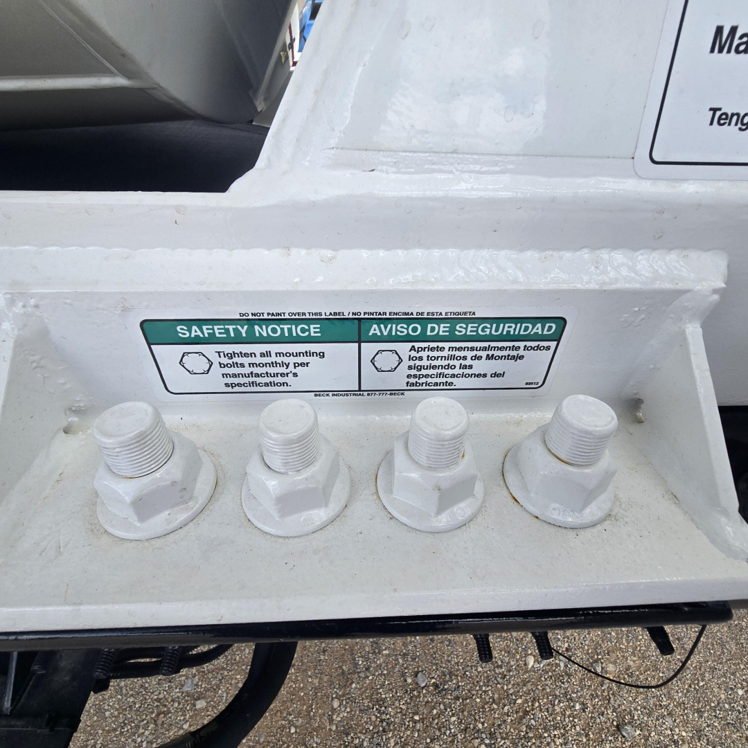 Safety notice label on a Mack mixer chassis with four bolt studs and a warning plaque in English and Spanish.