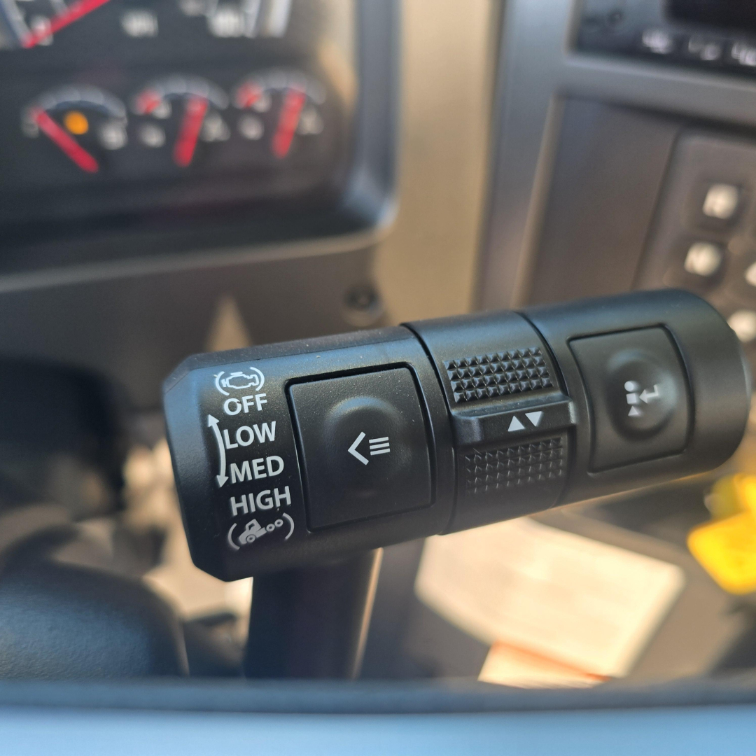 Steering column stalks inside Mack GR64B mixer truck showing light control with OFF LOW MED HIGH and wiper/washer symbols, dashboard and infotainment visible in background.