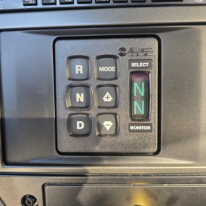 Cockpit console of a 2027 Mack GR64B showing N gear, R, N, D, plus Mode and Select buttons and a green NN indicator on the monitor.