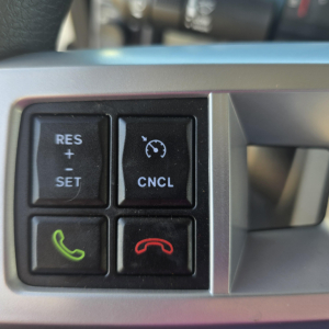 Truck cockpit steering wheel controls panel with RES + SET CNCL and phone icons in a Mack GR64B vehicle interior