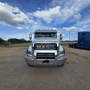Mack GR64B mixer truck front view showing chrome grille with MACK logo, large bumper, and headlights; clear sky and gravel lot background.