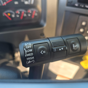 Steering column stalks inside Mack GR64B mixer truck showing light control with OFF LOW MED HIGH and wiper/washer symbols, dashboard and infotainment visible in background.