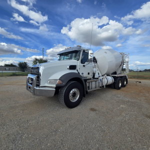 Concrete mixer truck in-service with large cement mixer mounted on chassis, Mack GR64B cab, white paint, front grille, and dual rear axles.
