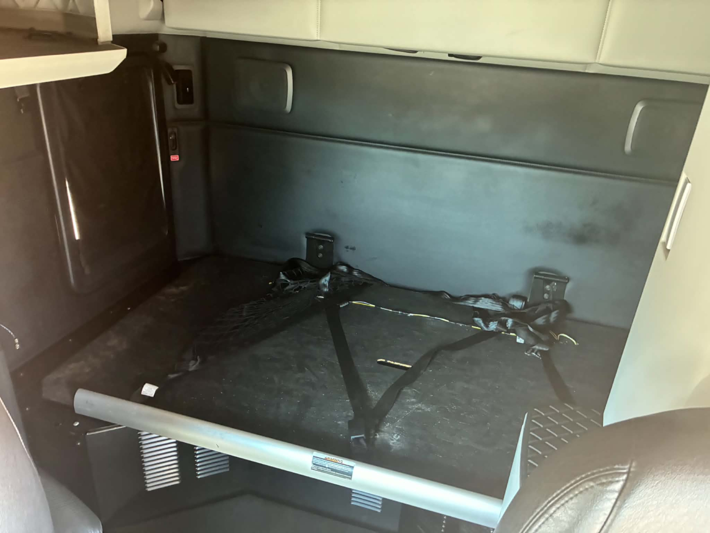 Kenworth T680 truck sleeper cab interior cargo area with harnesses and metal bar across floor.