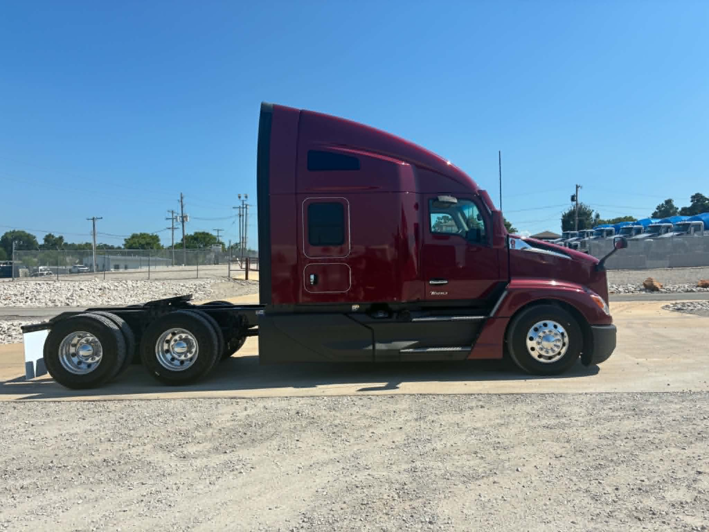 Kenworth T680 semi-truck side view, deep red cab with sleeper, black chassis, three rear axles, chrome wheels.