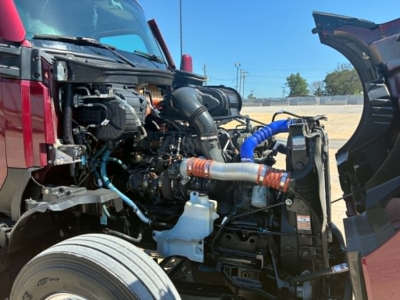 Kenworth T680 engine bay with exposed components and hoses showing cooling reservoir and various hoses.