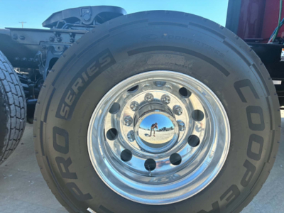 Wheel and tire close-up showing Goodyear tire with 'PRO SERIES' and 'COOPER' markings, chrome hubcap reflecting sky and ground.