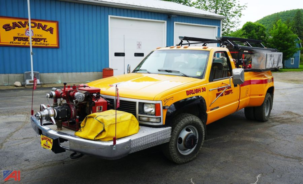 Front view of a yellow 1993 GMC Sierra SL Dually emergency pickup truck with roof light bar and siren equipment, front bumper hoses, and utility equipment mounted in a shop lot.
