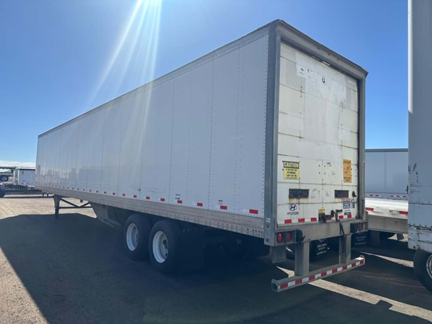 Hyundai air ride dry van trailer with white exterior, rear doors closed, dual rear axles, tandem wheels, and reflective safety tape along bottom edge.
